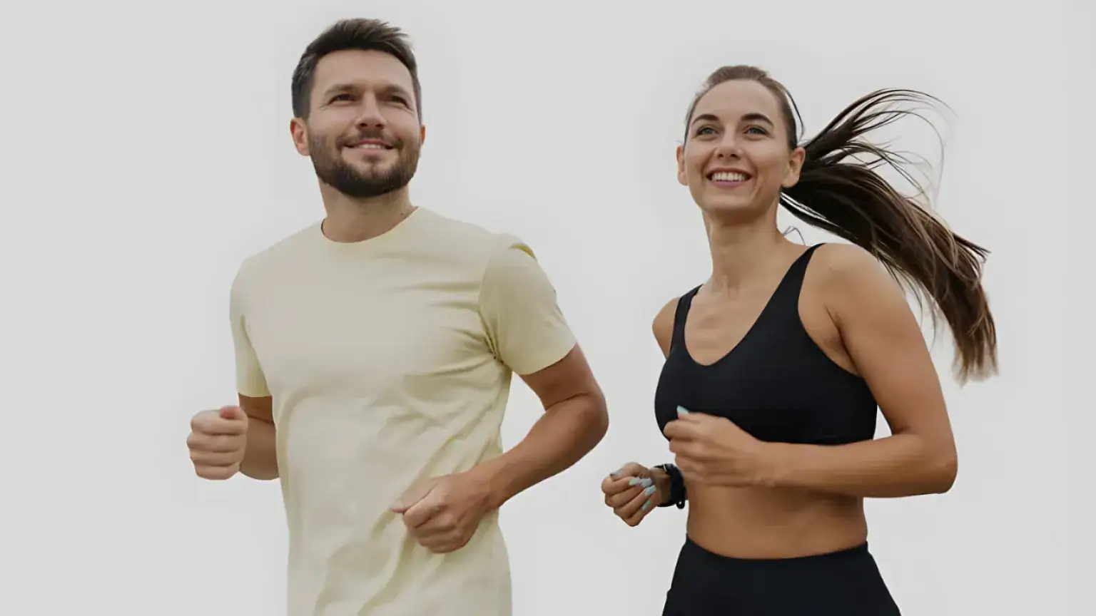 A smiling man and woman are jogging together outdoors, dressed in athletic wear, with the woman’s hair tied back. Both look ahead against a plain, light background—promoting vitality inspired by Castle Rock Hormone Health.